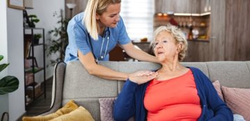 Caring nurse supports elderly woman in cozy living room setting A nurse provides comfort and care to an elderly woman at home.